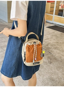 Detail of drawstring small crossbody bag with tennis racket charm and orange plaid pattern