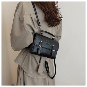 Macro shot of black leather handbag featuring dual buckle straps and embossed lettering