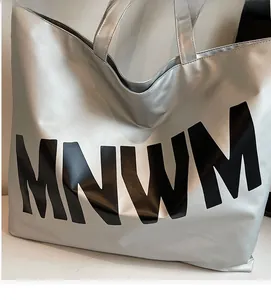 Close-up of silver tote bag featuring black MNWM letter print and double handles