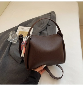 Détail du sac seau en cuir marron foncé avec un pendentif pompon tissé coloré