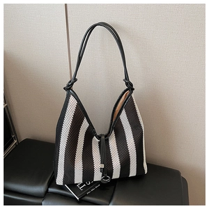 Detail of striped woven tote bag featuring black leather knotted handles and metal ring