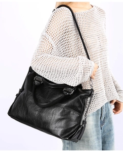 Close-up of black textured leather tote bag showing crossbody strap and side zipper detail