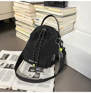 Detail of black drawstring crossbody bag with tennis racket charm and nylon texture
