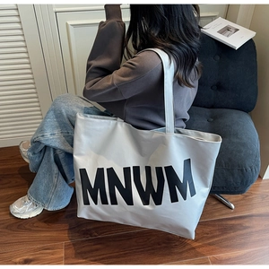 Close-up of a large grey minimalist tote bag with MNWM lettering held by a model