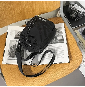 Detail of black nylon drawstring crossbody bag placed on a magazine and wooden chair