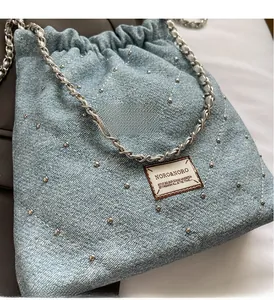 Detail of light blue denim drawstring bag with silver studs and chain strap