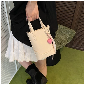 Détail du sac seau beige avec breloque cœur rose et doubles poignées sur modèle