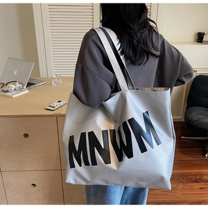 Detail of silver metallic tote bag with black MNWM lettering in a minimalist office setting