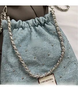 Detail of light blue denim bucket bag with metal rivets and chain strap textures