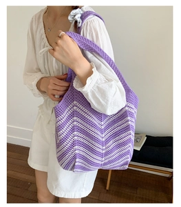 Dettaglio della borsa tote in maglia ondulata viola e bianca indossata da modella