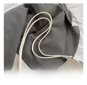 Détail des anses en cuir d'un sac seau blanc texturé orné de motifs de nœuds noirs