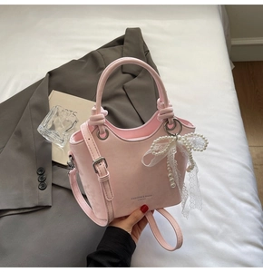 Détail du sac seau en cuir PU rose avec breloque nœud en dentelle et logo perlé