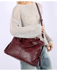 Dark red leather tote bag with tassel detail shown as a crossbody on a female model