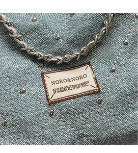 Close-up of light blue denim tote with quilted stitching and silver metal stud details