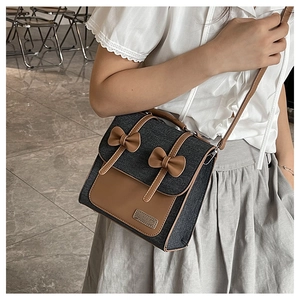 Detail of retro denim and brown leather crossbody bag with decorative bows and metal logo