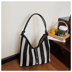Detail view of black and white striped mesh tote bag with leather trim on a wooden surface