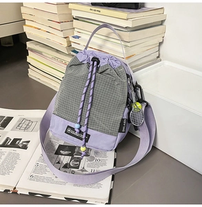 Detail of purple plaid drawstring bucket bag with mini tennis racket charm and broad strap