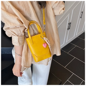 Détail du mini sac seau jaune avec pendentif cœur et cordon tressé sur une chemise