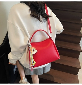 Détail d'un sac seau en cuir rouge avec charm arc-en-ciel porté par un mannequin