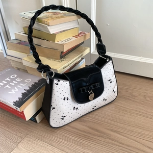 Detailansicht der Handtasche mit Schleifenmuster gewebtem Griff und Herzanhänger aus Metall