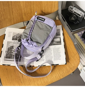 Detail of light purple canvas crossbody bag with drawstring pocket on a wooden chair