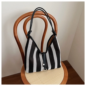 Close-up of black and white striped knit mesh tote bag on a rustic woven chair