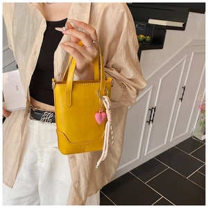 Détail du mini sac seau jaune en cuir lisse avec un pendentif en forme de cœur rose