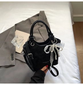 Détail du sac seau noir mat avec nœud en dentelle blanche et pendentifs en perles