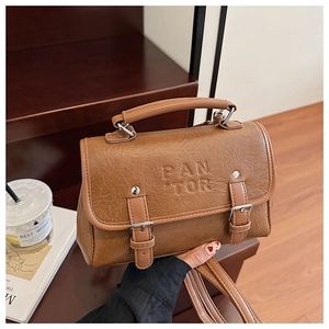 Detail view of brown leather bag with PAN TOR embossed logo and metallic buckle straps
