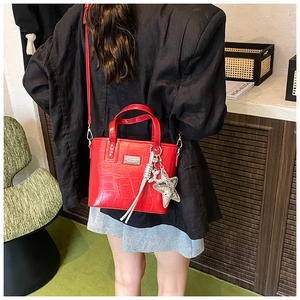 Detail of red crocodile textured tote bag with star charm and detachable strap