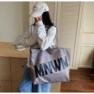 Detail of taupe large capacity tote bag with MNWM lettering and dual shoulder straps