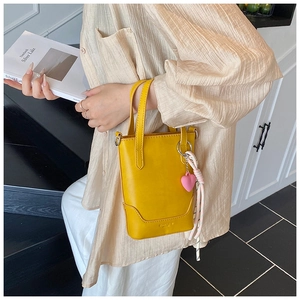 Détail du mini sac seau jaune avec breloque cœur rose et poignée en nœud tressé
