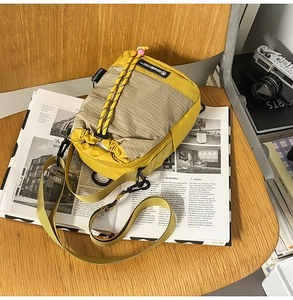 Detail of yellow and grey checkered nylon crossbody bag with camera and magazine background