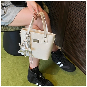Detailed view of a white crocodile embossed leather handbag with silver star charm accessory