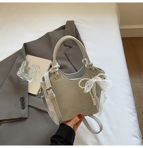 Détail du sac seau gris-vert clair avec nœud en dentelle et perles sur un blazer gris