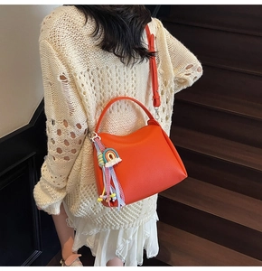 Détail d'un sac seau en cuir orange vif avec un pendentif arc-en-ciel à pompons