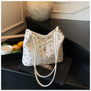 Détail du sac cabas blanc avec imprimés nœuds noirs et pendentif cœur argenté