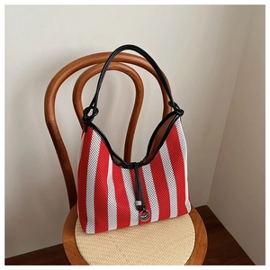 Detail of red striped tote bag with black leather handle and metallic ring on wooden chair
