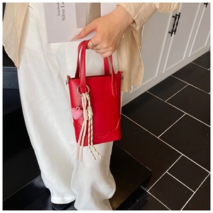 Détail du mini sac seau rouge avec pendentif cœur et cordes tenu par un mannequin