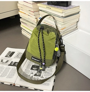 Close-up of olive green drawstring crossbody bag with mesh texture and tennis charm