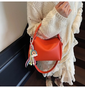 Détail d'un sac seau en cuir orange avec un gland arc-en-ciel porté par un mannequin