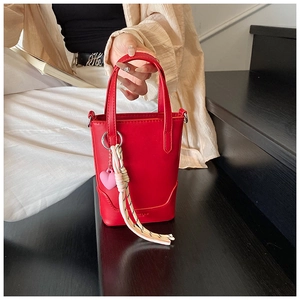 Détail du sac seau rouge avec pendentif cœur et corde tressée sur fond de rue