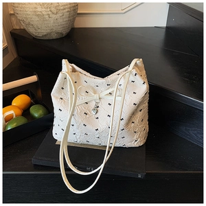 Détail d'un sac cabas blanc avec motifs nœuds noirs et pendentif cœur sur escalier