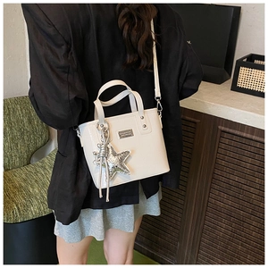 Detail of white crocodile-embossed tote bag featuring a sparkling silver star charm