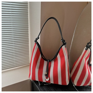 Detailed view of red and white striped woven tote bag with black leather strap on a table