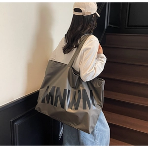 Close-up of olive green tote bag with MNWM lettering on a model's shoulder