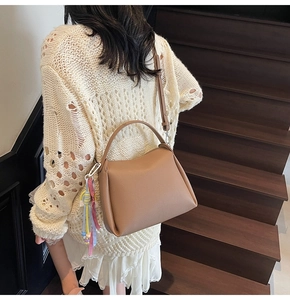 Détail du sac seau en cuir camel avec pompon tressé sur un escalier en bois rustique