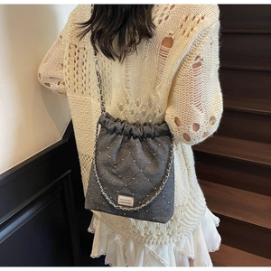 Detail shot of grey quilted shoulder bag with silver studs and chain strap worn by model
