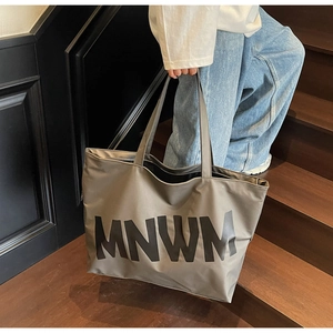 Detail of dark grey tote bag with MNWM lettering and long handles on wooden stairs