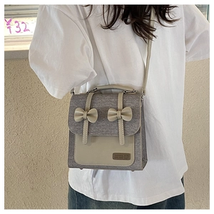 Detail of grey fabric and beige leather patchwork bag featuring two decorative bows